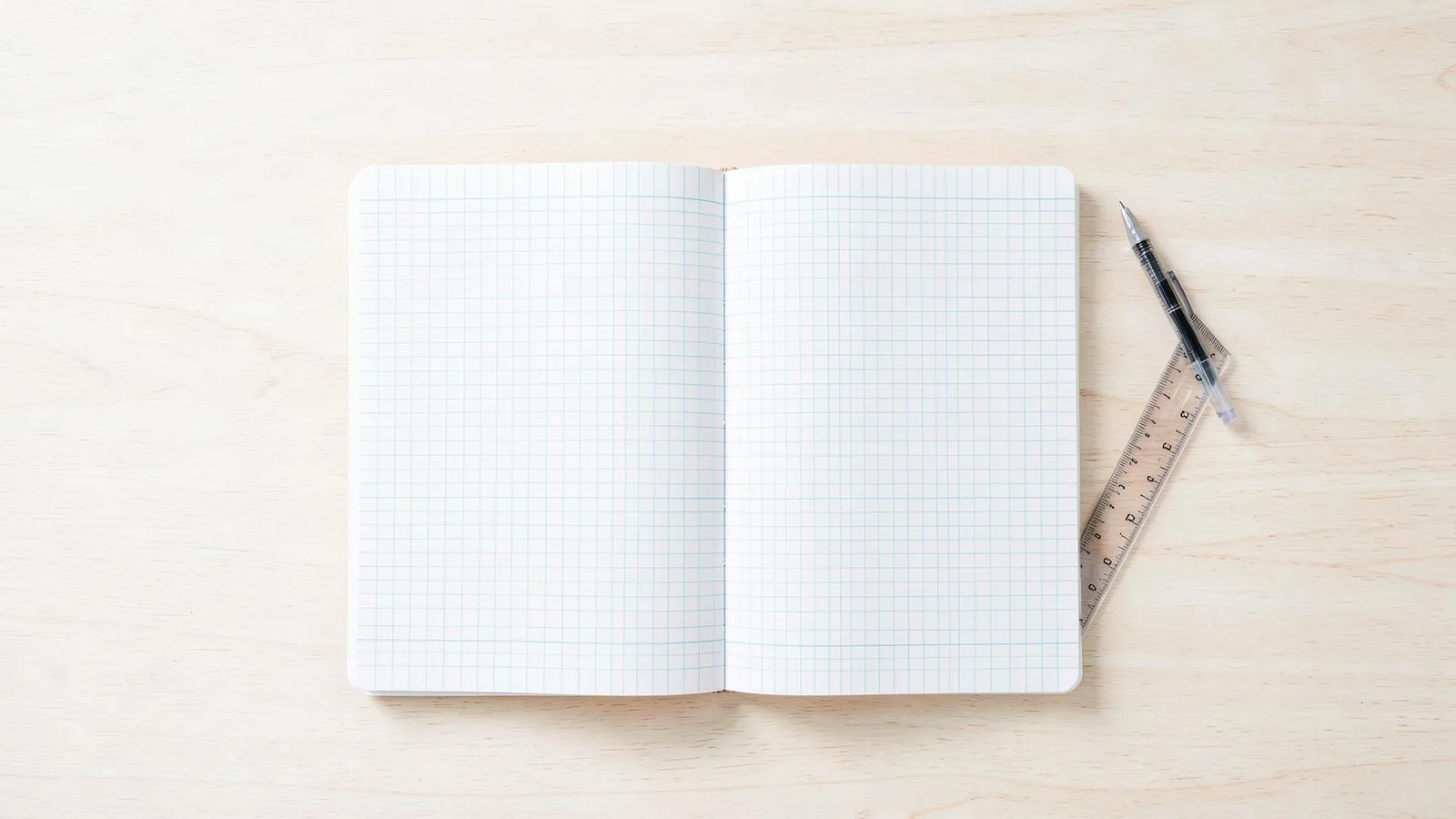Un cahier ouvert, un stylo et une règle posés sur un bureau clair, vus de dessus