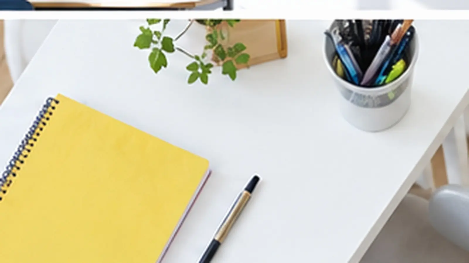 Vue de dessus d'un bureau blanc avec un cahier jaune, des stylos et une plante verte